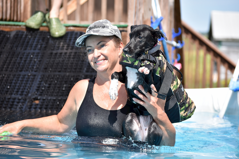 Happy owner in a pool praising dog for swimming